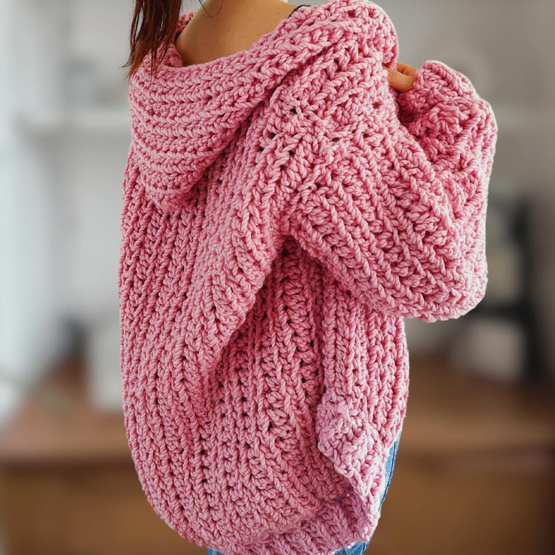 Op de afbeelding: Een roze gebreide cardigan met een capuchon. De cardigan is gemaakt met een textuur-steek en heeft een losse pasvorm.