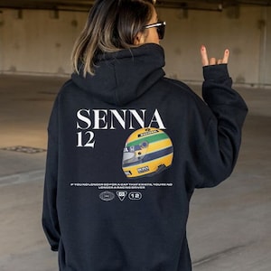 May include: Black hooded sweatshirt with a white graphic print of a racing helmet and the text "SENNA 12" and the quote "If you no longer go for a gap that exists, you're no longer a racing driver".