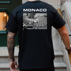 Peut inclure: T-shirt noir avec un imprim&eacute; graphique blanc d'un circuit de course avec des voitures. Le texte "MONACO" est imprim&eacute; deux fois sur le t-shirt, et le texte "MONTE CARLO CIRCUIT DE MONACO" est imprim&eacute; sous le graphique.