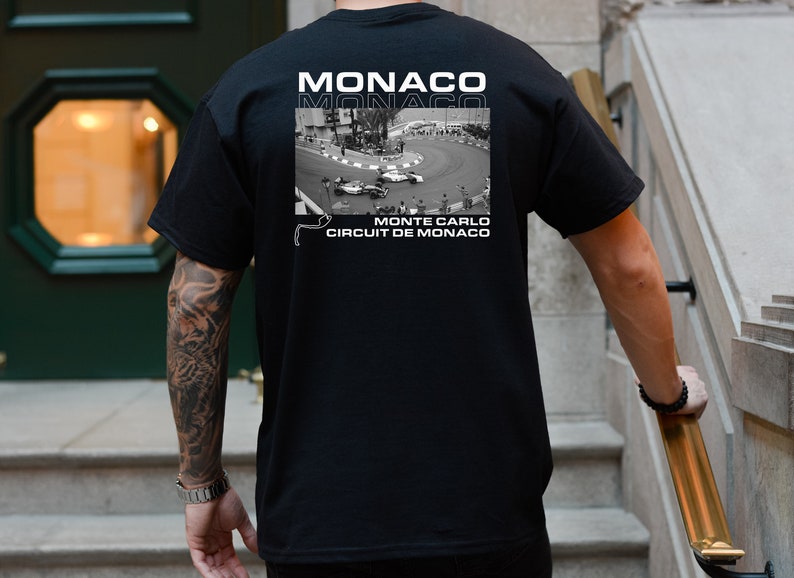 Peut inclure: T-shirt noir avec un imprim&eacute; graphique blanc d'un circuit de course avec des voitures. Le texte "MONACO" est imprim&eacute; deux fois sur le t-shirt, et le texte "MONTE CARLO CIRCUIT DE MONACO" est imprim&eacute; sous le graphique.