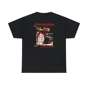 May include: Black t-shirt with a graphic of Ayrton Senna in a red and white race car. The text "Ayrton Senna" and "1960" are printed on the shirt.