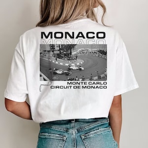 Peut inclure: T-shirt blanc avec un imprim&eacute; graphique noir et blanc d'une voiture de course sur un circuit. Le texte "MONACO" est imprim&eacute; en noir sur le t-shirt, ainsi que le texte "MONTE CARLO CIRCUIT DE MONACO".