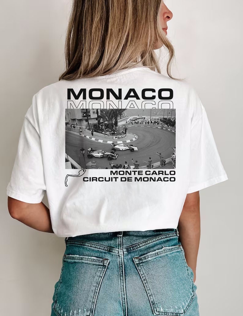 Peut inclure: T-shirt blanc avec un imprim&eacute; graphique noir et blanc d'une voiture de course sur un circuit. Le texte "MONACO" est imprim&eacute; en noir sur le t-shirt, ainsi que le texte "MONTE CARLO CIRCUIT DE MONACO".