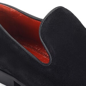 Op de afbeelding: Zwarte su&egrave;de loafers met een rode leren voering. De loafers hebben een spitse neus en een lage hak.
