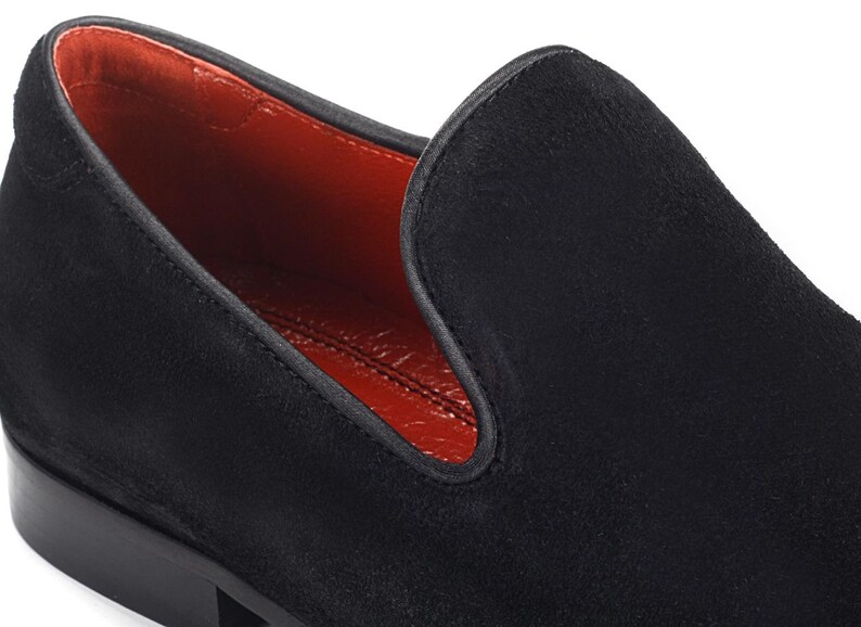 Op de afbeelding: Zwarte su&egrave;de loafers met een rode leren voering. De loafers hebben een spitse neus en een lage hak.