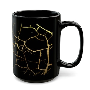 Może przedstawiać: Czarny kubek ceramiczny z wzorem złotego pęknięcia. Kubek ma duży uchwyt.