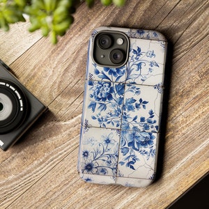 Può includere: Una custodia per telefono bianca e blu con un motivo floreale. La custodia è progettata per adattarsi a uno smartphone con una fotocamera a tre obiettivi.