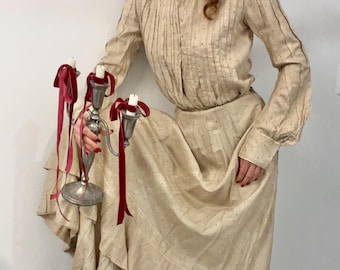 May include: A cream-coloured vintage dress with small black dots and vertical stripes. The dress has long sleeves and a tiered skirt. A silver candelabra with red ribbons and lit candles is in the foreground.