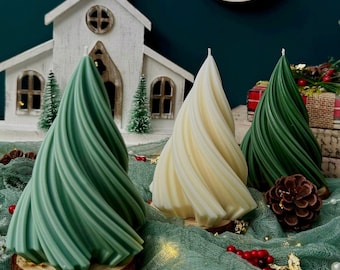 May include: Three Christmas tree-shaped candles, one green, one white, and one green, on a green mesh surface with gold glitter and a wooden church in the background.