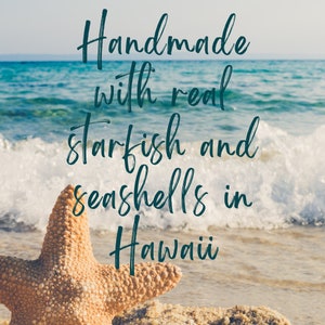 Pu&ograve; includere: Primo piano di una stella marina beige su una spiaggia sabbiosa con onde dell'oceano sullo sfondo. L'immagine contiene il testo "Handmade with real starfish and seashells in Hawaii."
