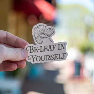 May include: A white sticker with a green ginkgo leaf design and the text "Be-Leaf in Yourself".