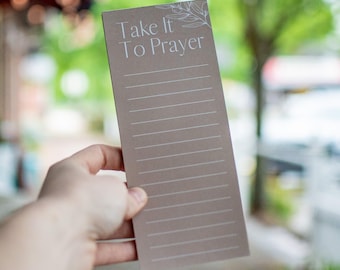May include: A brown paper notepad with a white floral design and the text "Take It To Prayer".