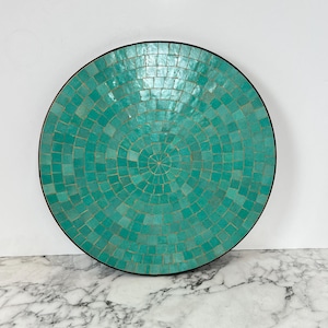 Könnte beinhalten: Ein rundes, türkisfarbenes Mosaiktablett mit schwarzem Rand. Das Tablett besteht aus kleinen quadratischen Fliesen, die in einem konzentrischen Kreis angeordnet sind.