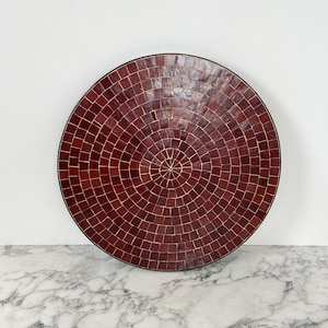 May include: A round, red mosaic tile tray with a dark brown rim. The tray is made of small, square tiles that are arranged in a concentric circle pattern.
