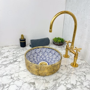May include: A gold and blue ceramic vessel sink with a decorative pattern. The sink is on a white marble countertop with a gold faucet.