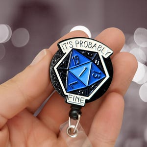 Peut inclure: Un enrouleur de badge noir et blanc avec le texte "IT'S PROBABLY FINE". Le badge présente un design de dé D20 bleu et blanc. L'enrouleur a un cordon noir et une sangle en plastique transparent.