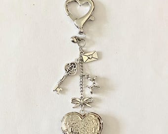 May include: Silver heart-shaped locket keychain with a key, envelope, and bow charms. The locket has an intricate floral design.