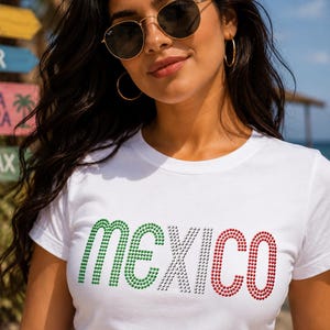 May include: A white short-sleeved t-shirt featuring the word MEXICO spelled out in small, sparkling rhinestones. The letters M and E are green, the letter X is white, and the letters I, C, and O are red, mimicking the colors of the Mexican flag.