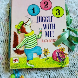 Puede incluir: Un libro infantil vintage titulado "Juggle With Me! A Counting Book" que presenta a un zorro haciendo malabares con pelotas de colores con los números 1, 2 y 3. El libro es rosa con ilustraciones verdes y amarillas.