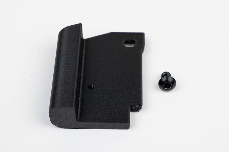 May include: A black plastic part with a rounded edge and a hole in the top. A black screw is included.