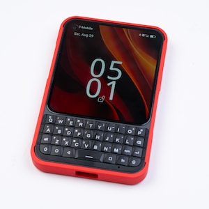 Könnte beinhalten: Ein Smartphone mit einer leuchtend roten Schutzhülle und einer physischen QWERTY-Tastatur. Der Bildschirm zeigt den Text T-Mobile, Sat, Aug 29 und die Uhrzeit 05:01 mit einem Schloss-Symbol. Das Gerät hat eine schwarze Tastatur mit weißer Schrift.