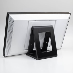 May include: A white digital picture frame with a black stand. The frame has a speaker grille on the side and a small black stand.