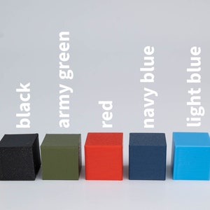 May include: Eight small, square blocks in different colors, arranged in a row from left to right: yellow, black, army green, red, navy blue, light blue, and white. The blocks are labeled with their corresponding colors.