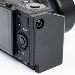 May include: A black camera with a lens attached and a black protective case. The camera has a screen on the back and various buttons and dials.