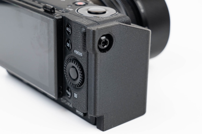 May include: A black camera with a lens attached and a black protective case. The camera has a screen on the back and various buttons and dials.
