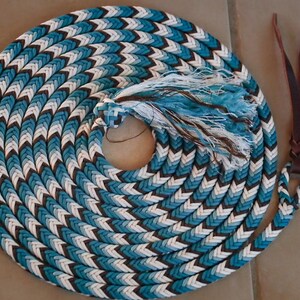 May include: Coiled turquoise, white, and brown rope with a braided pattern. The rope has a tassel and leather strap attached. The rope is designed for equestrian use.