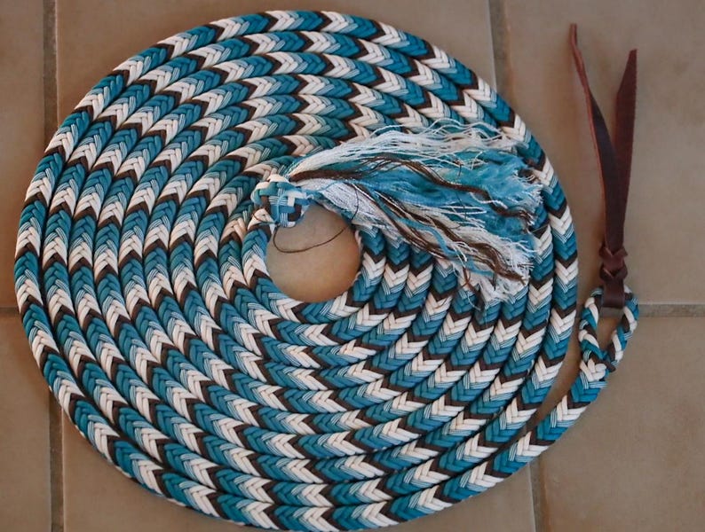 May include: Coiled turquoise, white, and brown rope with a braided pattern. The rope has a tassel and leather strap attached. The rope is designed for equestrian use.