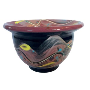 May include: A small, hand-painted ceramic bowl with a black base and a pink, yellow, and blue swirl design.