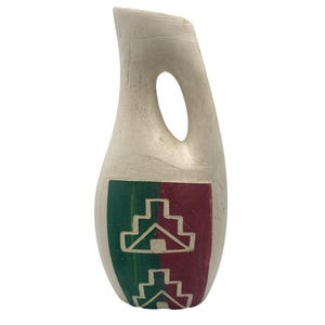 May include: A tall, off-white ceramic vase with a smooth, matte finish and a single integrated handle near the top. The lower section features a rectangular panel divided into green and maroon halves, decorated with two white, stepped geometric patterns.