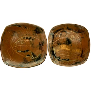 May include: Two square ceramic plates with brown and black glaze. The plates have a raised design of stylized fish and other abstract shapes.