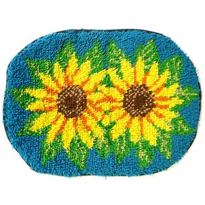 May include: A blue oval rug with two yellow sunflowers with brown centers. The sunflowers are surrounded by green leaves.