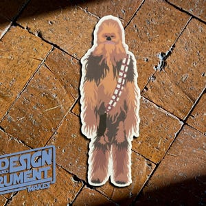 May include: A brown and white Chewbacca character sticker. The sticker is on a brown tiled floor.