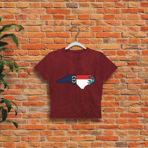 May include: A maroon cropped t-shirt featuring a graphic of the state of North Carolina with the state flag superimposed on the outline.