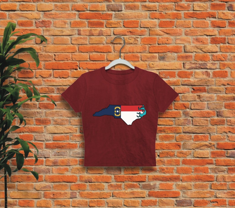 May include: A maroon cropped t-shirt featuring a graphic of the state of North Carolina with the state flag superimposed on the outline.
