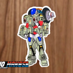 May include: A sticker of a cartoon robot wearing a blue helmet and a red and white suit. The robot is holding a large, gray, cylindrical object with a black tire on the end. The robot has a number "21" on its chest and the letters "MB" on its legs.