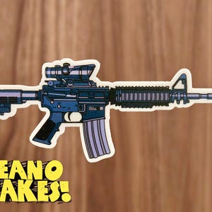 May include: A blue and black sticker of an AR-15 style rifle with a red and black scope. The sticker has the text "DEANO MAKES!" printed on it.