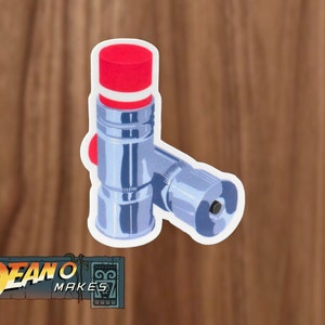 May include: A silver-colored valve with a red and white top. The valve has a round knob on the side.