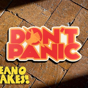 May include: A red and orange sticker with the text "DON'T PANIC" in a bold, retro font. The sticker is on a brown tiled surface. The text "DEANO MAKES!" is in yellow below the sticker.