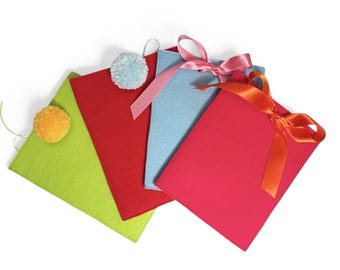 Può includere: Quattro sacchetti regalo in feltro con pon pon e fiocchi. I sacchetti sono verde, rosso, blu e rosa.