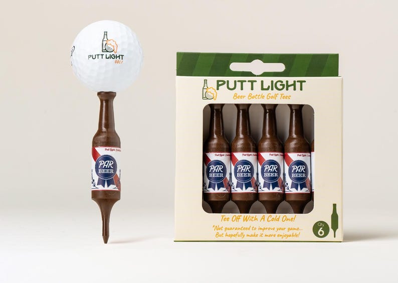 Pu&ograve; includere: Una pallina da golf bianca con il logo Putt Light appoggiata su un tee da golf marrone a forma di bottiglia di birra. Accanto c'&egrave; una scatola contenente sei tee da golf marroni a forma di bottiglia di birra etichettati Par Beer. La confezione riporta il testo Putt Light Beer Bottle Golf Tees.
