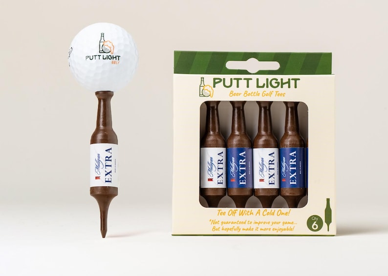 Pu&ograve; includere: Una pallina da golf bianca con il logo Putt Light Golf &egrave; posizionata su un tee da golf marrone a forma di bottiglia di birra. Accanto, una scatola di cartone contiene quattro tee marroni identici etichettati Mulligan Extra e Putt Light.