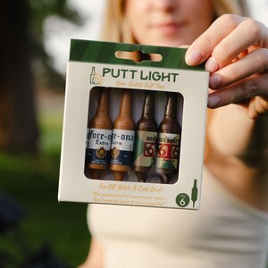 Pu&ograve; includere: Una scatola di cartone rettangolare contenente sei tee da golf a forma di bottiglie di birra in miniatura. La confezione riporta il testo PUTT LIGHT, Beer Bottle Golf Tees e Tee Off With A Cold One! Le bottiglie hanno etichette fore-ore-ona e DOS BOGEY.