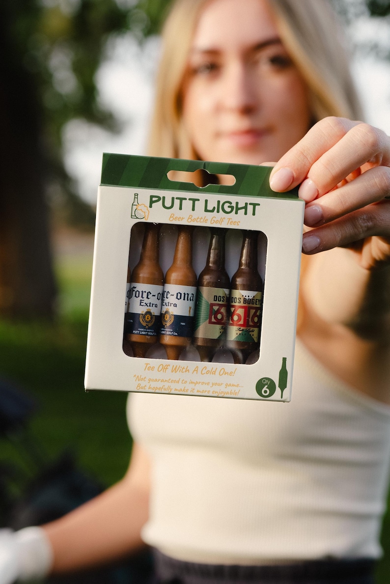 Pu&ograve; includere: Una scatola di cartone rettangolare contenente sei tee da golf a forma di bottiglie di birra in miniatura. La confezione riporta il testo PUTT LIGHT, Beer Bottle Golf Tees e Tee Off With A Cold One! Le bottiglie hanno etichette fore-ore-ona e DOS BOGEY.