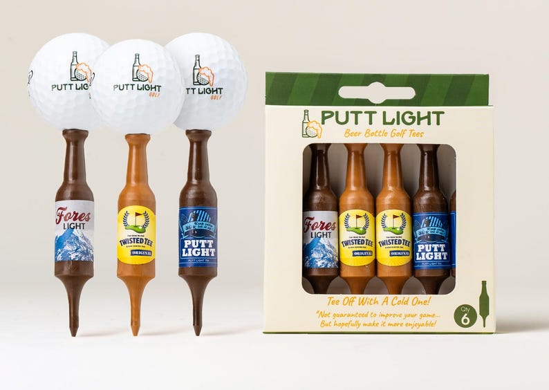Pu&ograve; includere: Tre palline da golf bianche appoggiate su tee da golf marroni a forma di bottiglia di birra, accanto a una scatola di cartone contenente sei tee identici. La confezione riporta il testo "PUTT LIGHT Beer Bottle Golf Tees" e "Tee Off With A Cold One".