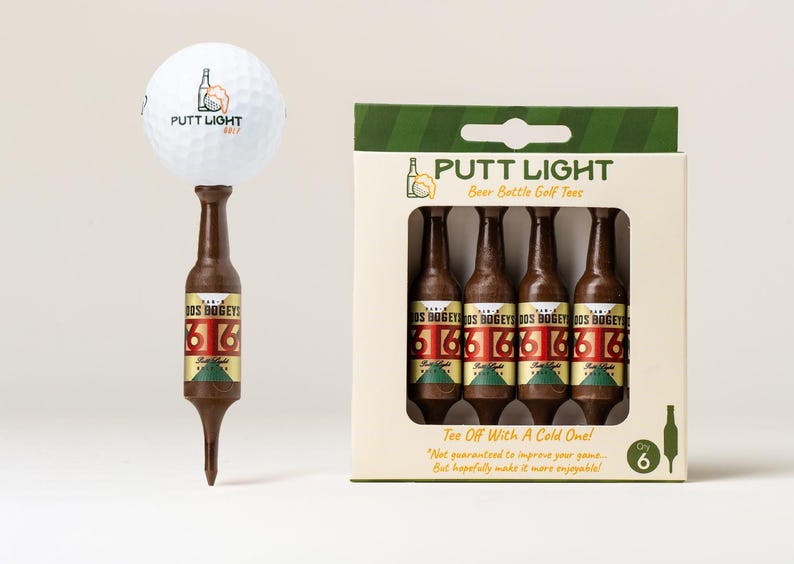 Pu&ograve; includere: Una pallina da golf bianca con il logo Putt Light Golf &egrave; posizionata sopra un tee da golf marrone a forma di bottiglia di birra. Accanto, una scatola di cartone contiene quattro tee identici a forma di bottiglia, etichettati Dos Bogeys e 6.