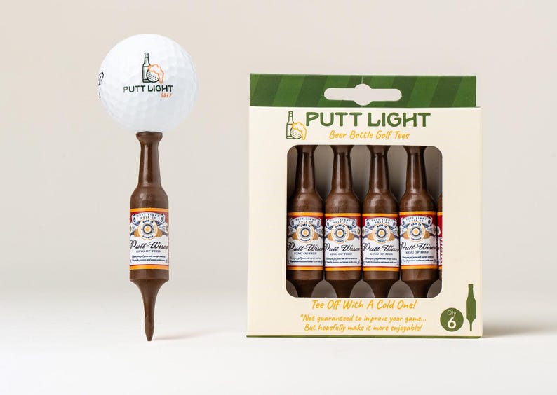 Pu&ograve; includere: Una pallina da golf bianca con il logo Putt Light Golf &egrave; posizionata sopra un tee da golf marrone a forma di bottiglia di birra. Accanto, una scatola di cartone contiene cinque tee marroni a forma di bottiglia, etichettati Putt Light.